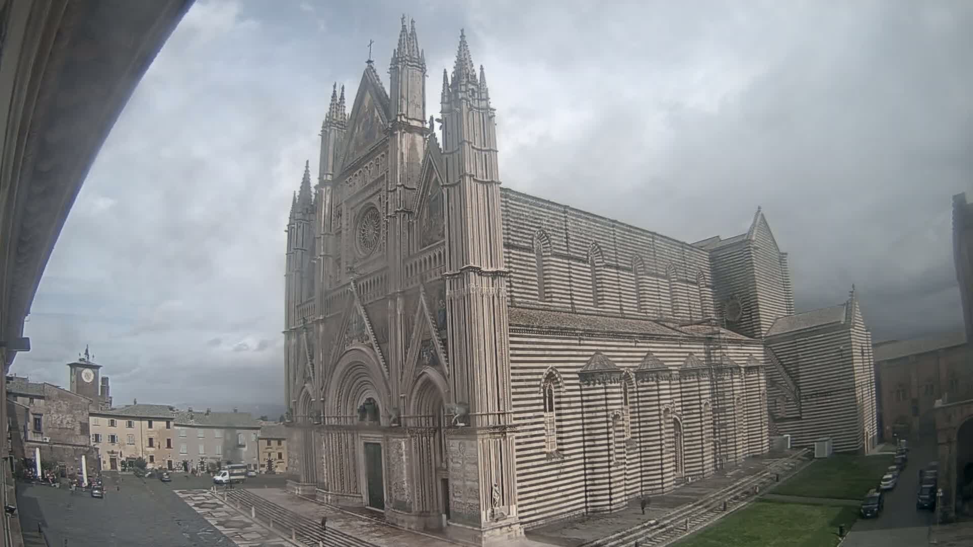 A large, striped cathedral stands in a town square under a cloudy sky.