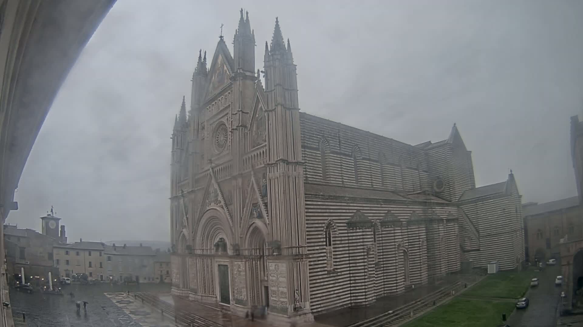 A large, striped cathedral stands in a town square on a rainy day.