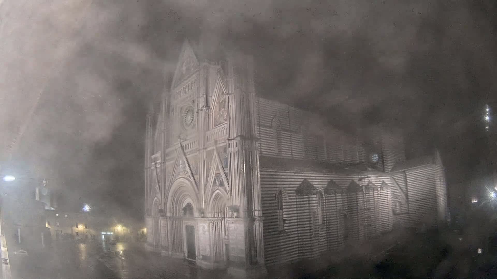 A large, gothic-style cathedral stands in the midst of a heavy, nighttime fog and rain.