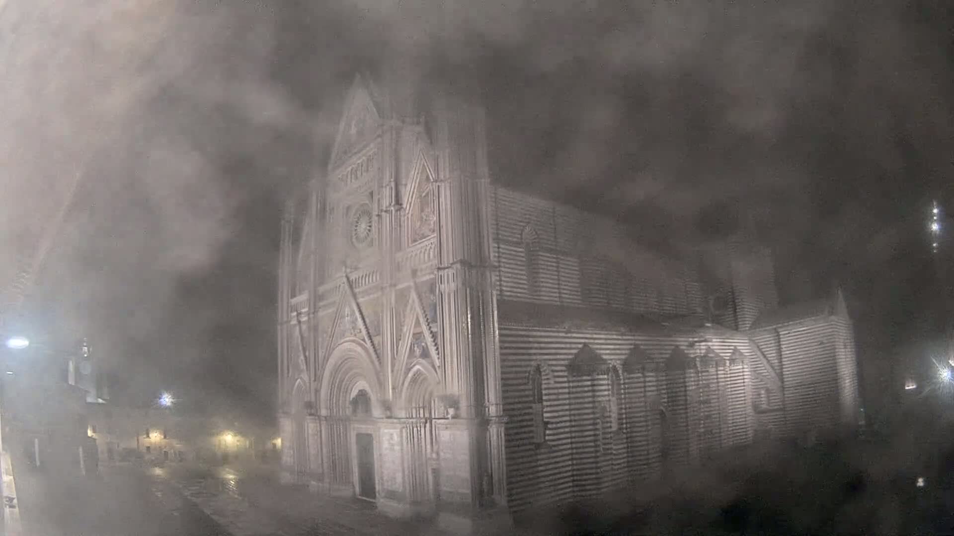 A large, ornate stone cathedral is partially obscured by a thick fog at night.