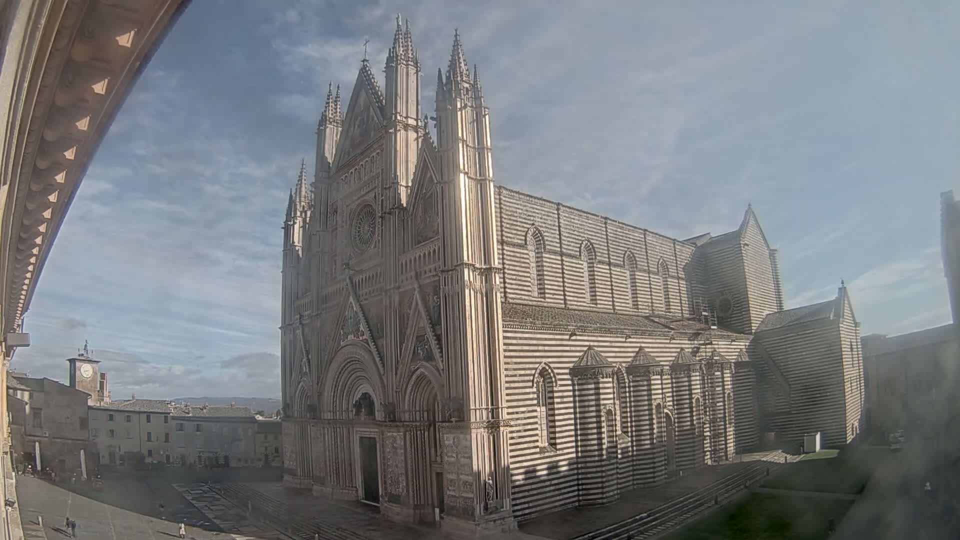 A large, striped cathedral stands in a town square under a mostly clear sky.