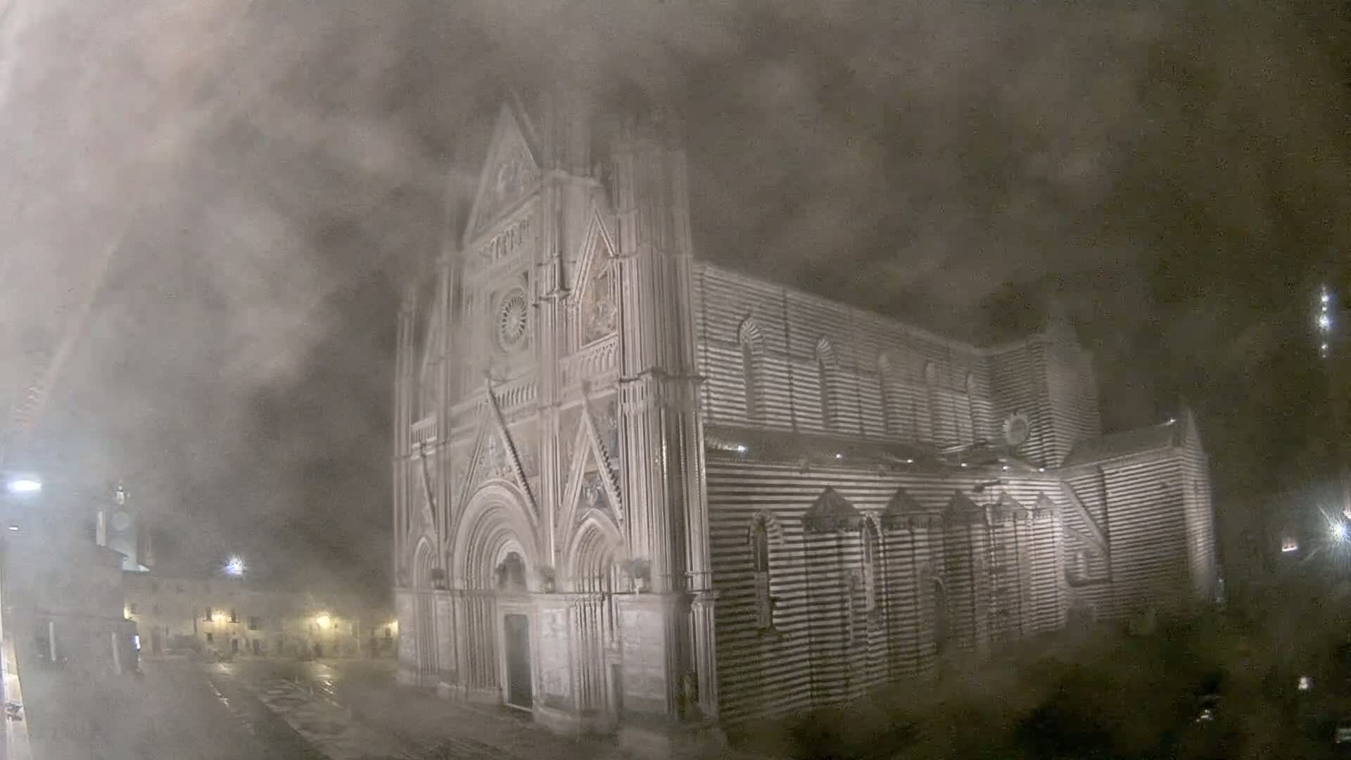 A large, striped cathedral stands in a town square at night, obscured by a heavy fog or snowstorm.