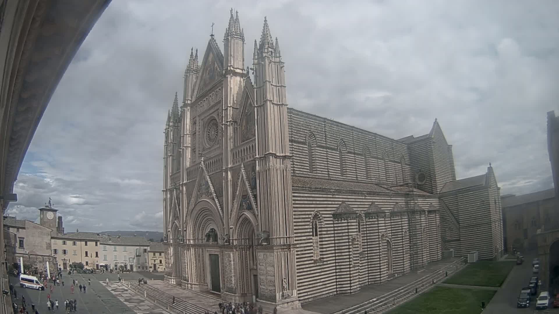 A large, striped stone cathedral stands in a town square under a cloudy sky.