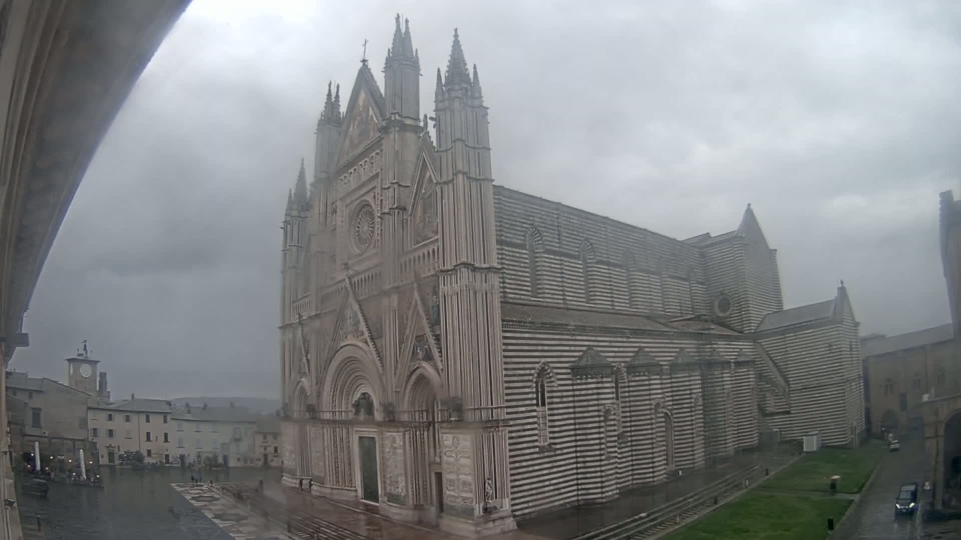 A large, striped cathedral stands in a town square on a rainy day.