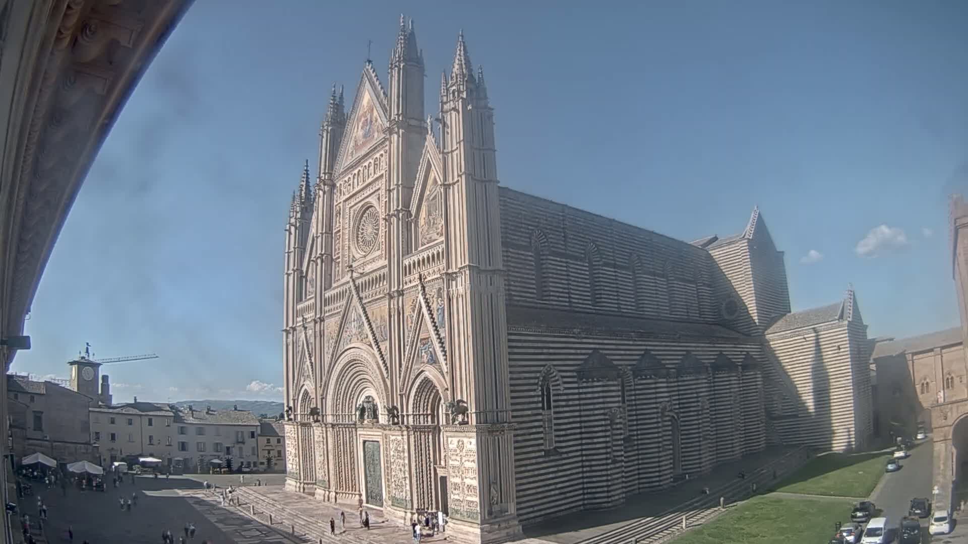 A large, ornate cathedral with black and white striped exterior stands in a town square on a sunny day.