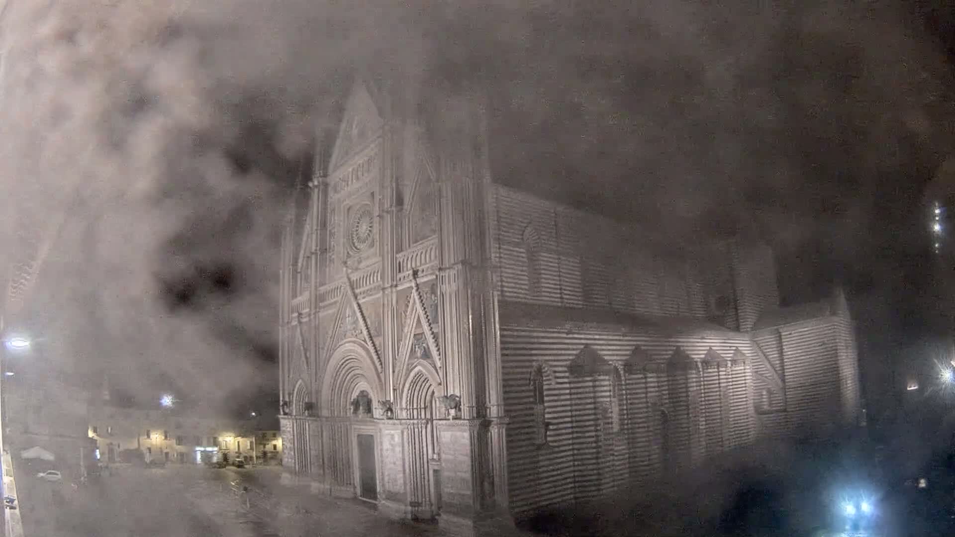 A large, striped stone cathedral is partially obscured by a thick fog at night.