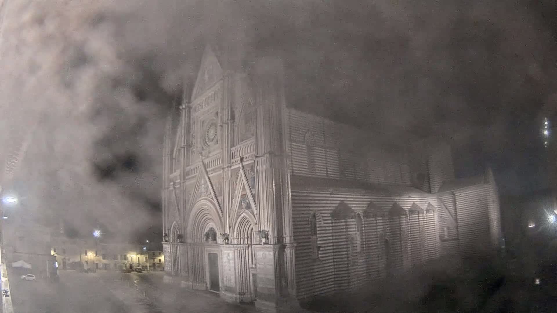 A large, striped stone cathedral is partially obscured by a thick fog at night.