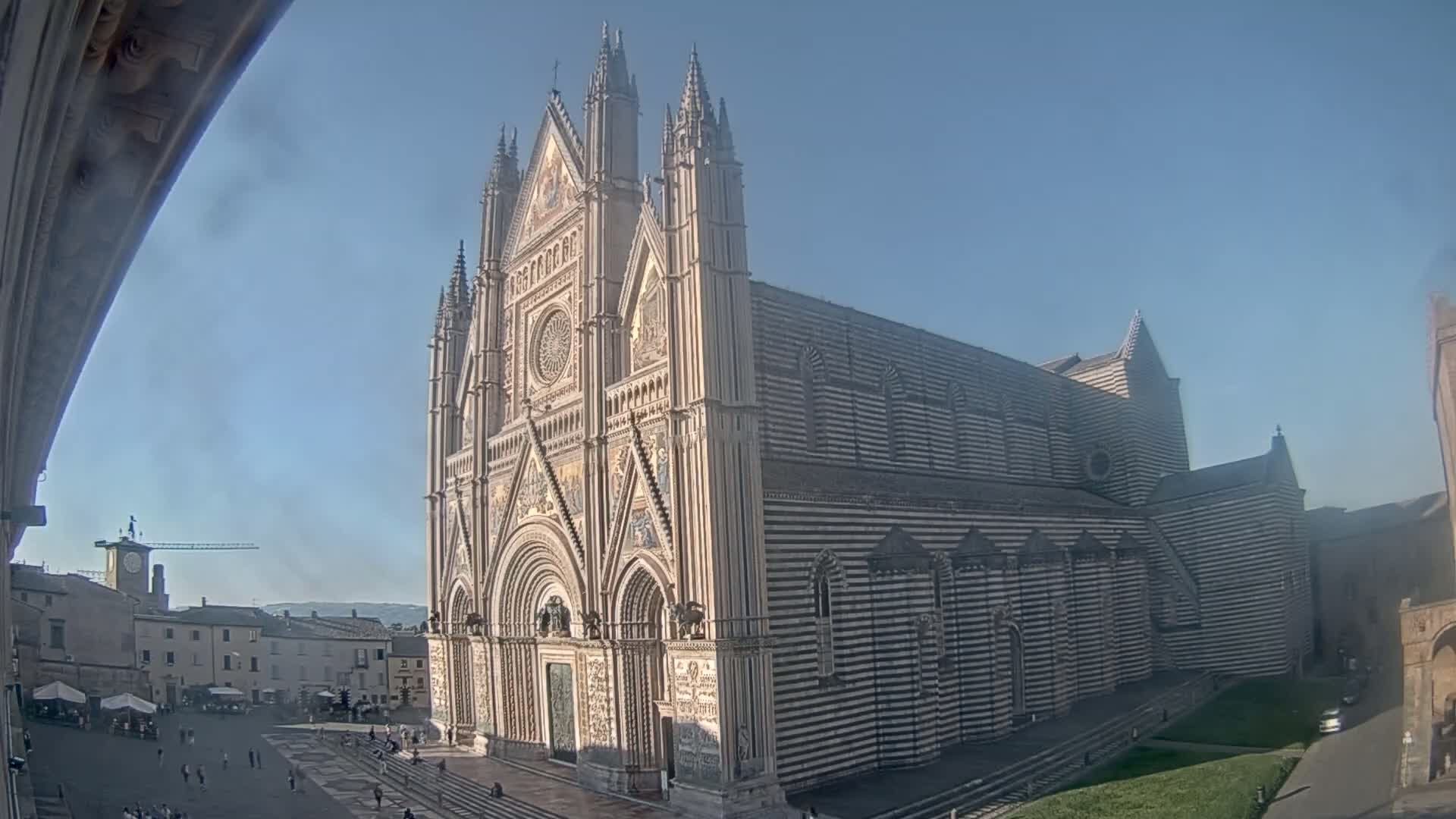 A large, striped cathedral stands in a town square on a clear, sunny day.