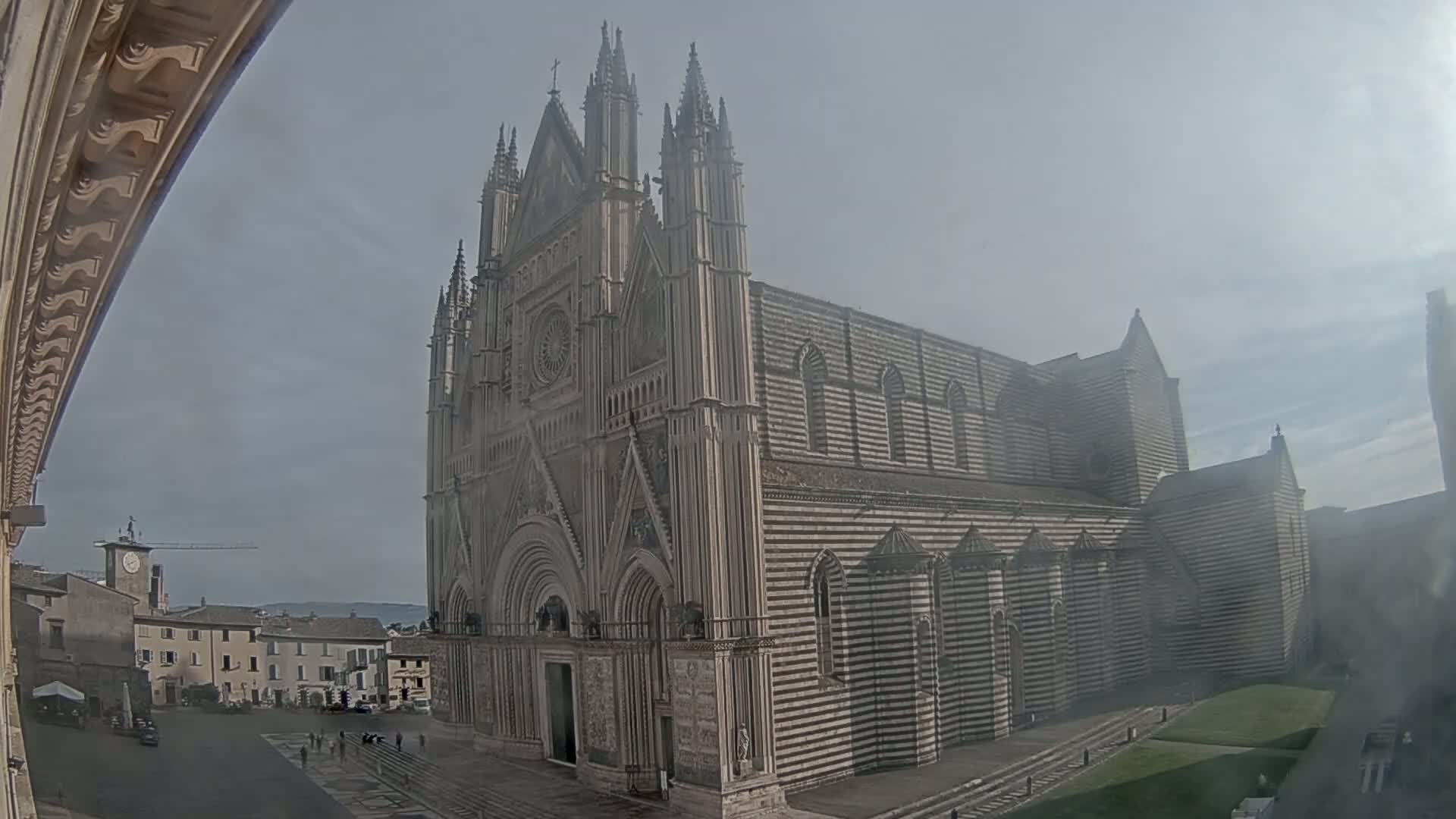 A large, striped stone cathedral stands in a town square on a hazy day.