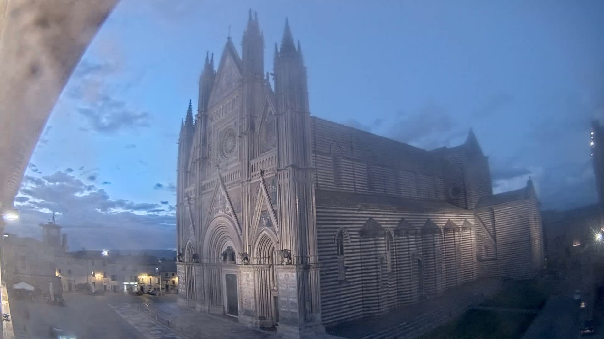 A large, striped cathedral stands in a town square on a misty evening.