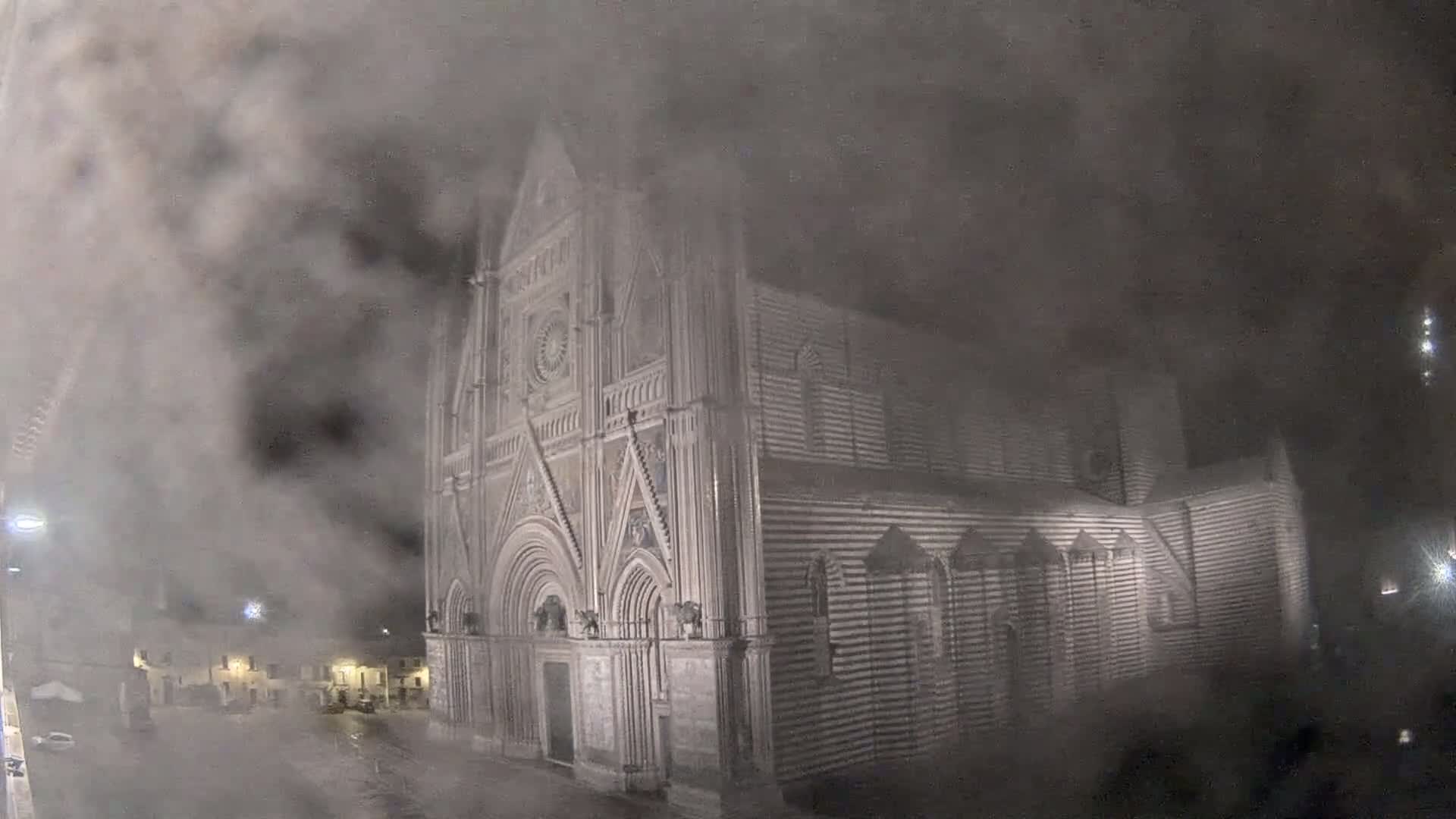 A large, ornate stone cathedral is partially obscured by a thick fog at night.