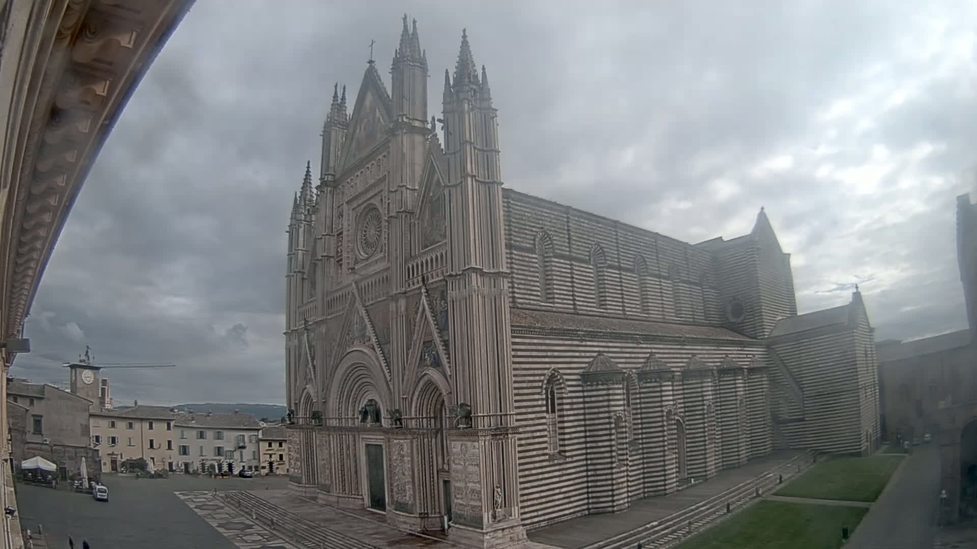 A large, striped cathedral stands in a town square under a cloudy sky.