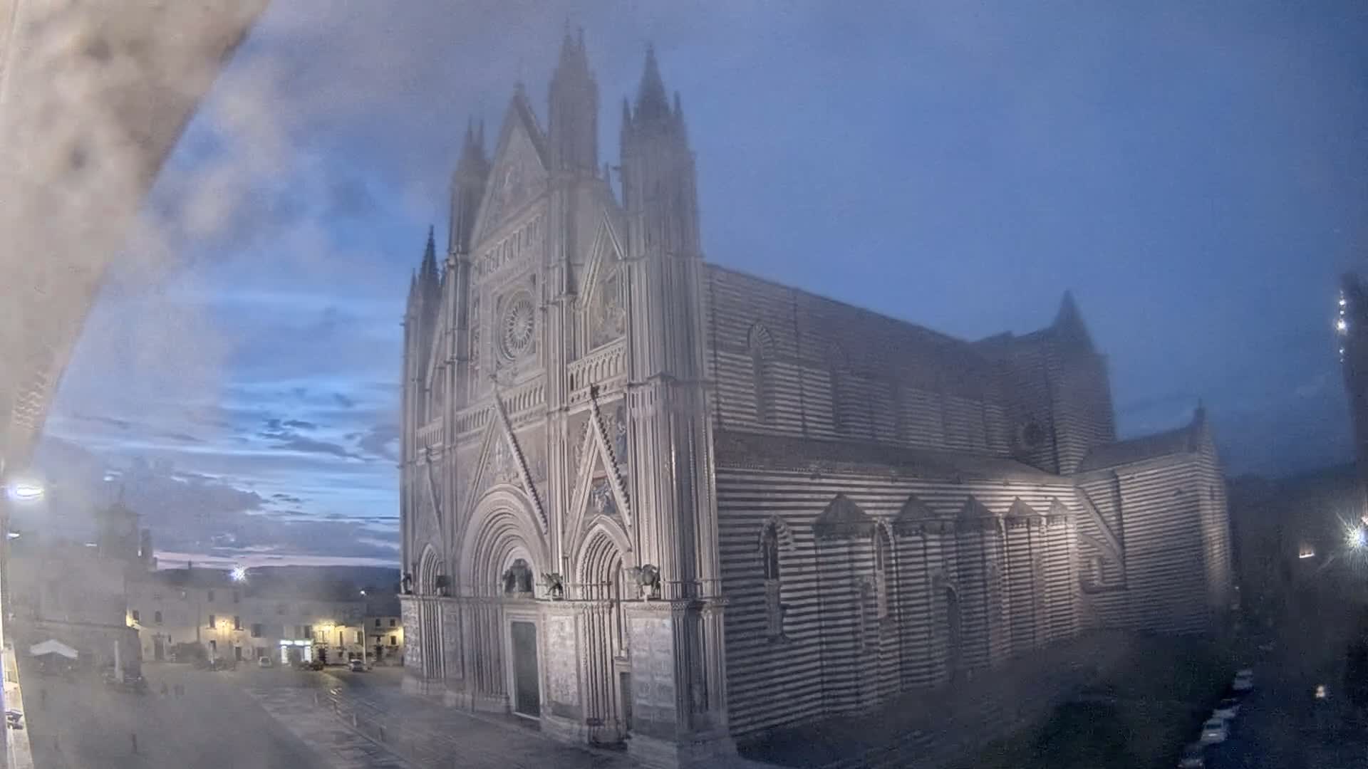 A large, striped cathedral stands in a town square under a hazy, twilight sky.