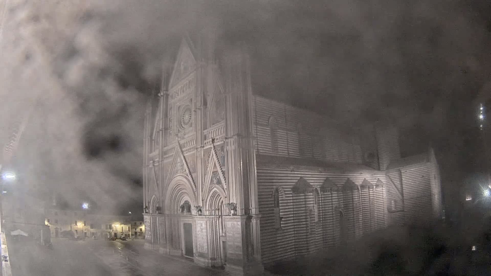 A large, striped stone cathedral is partially obscured by heavy fog at night.