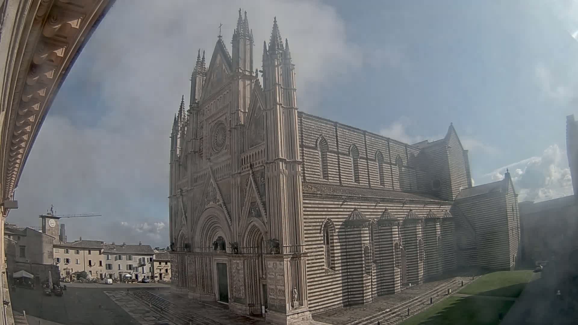 A large, striped stone cathedral stands in a town square on a partly cloudy day.