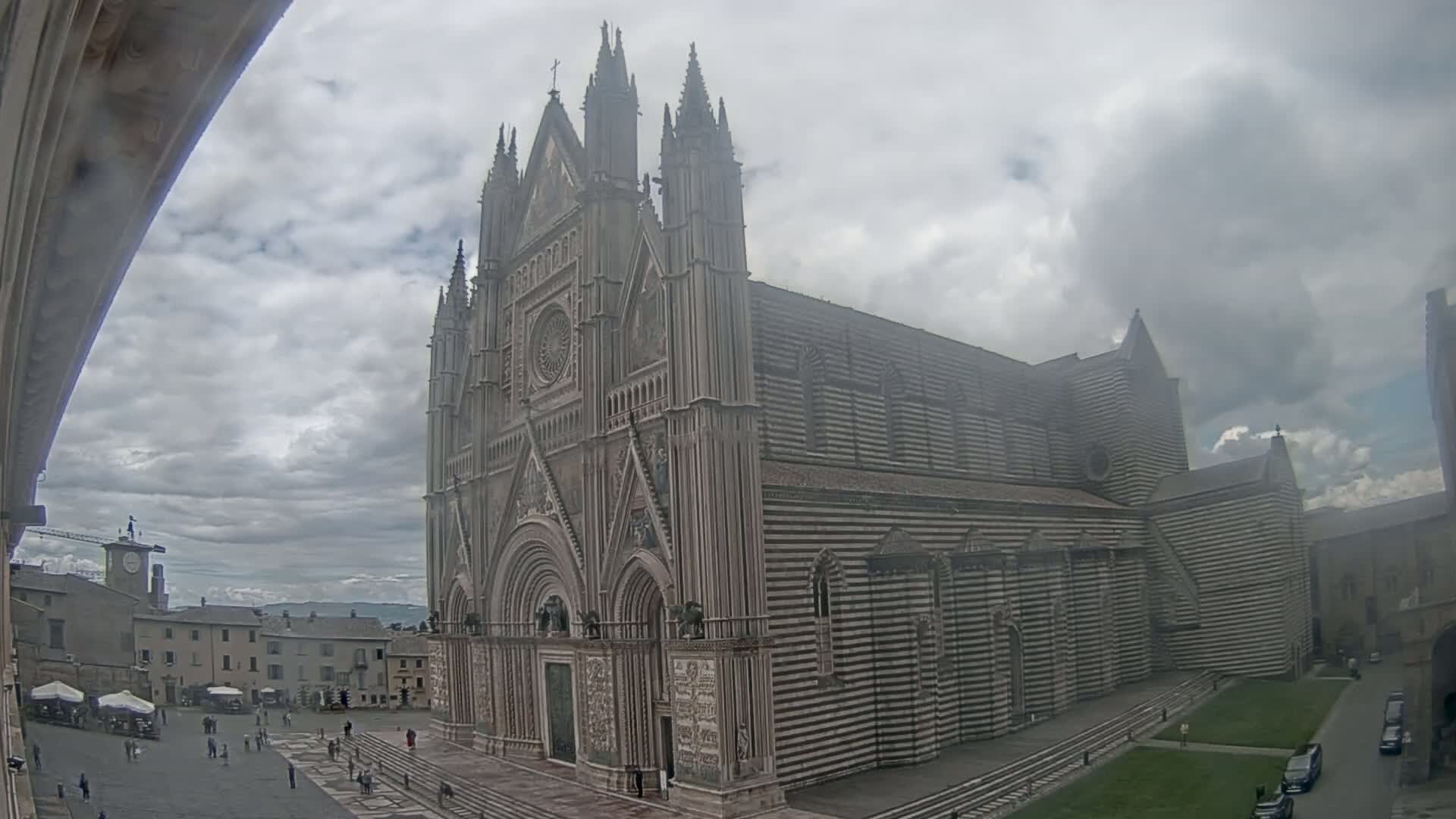 A large, striped cathedral stands in a town square under a cloudy sky.