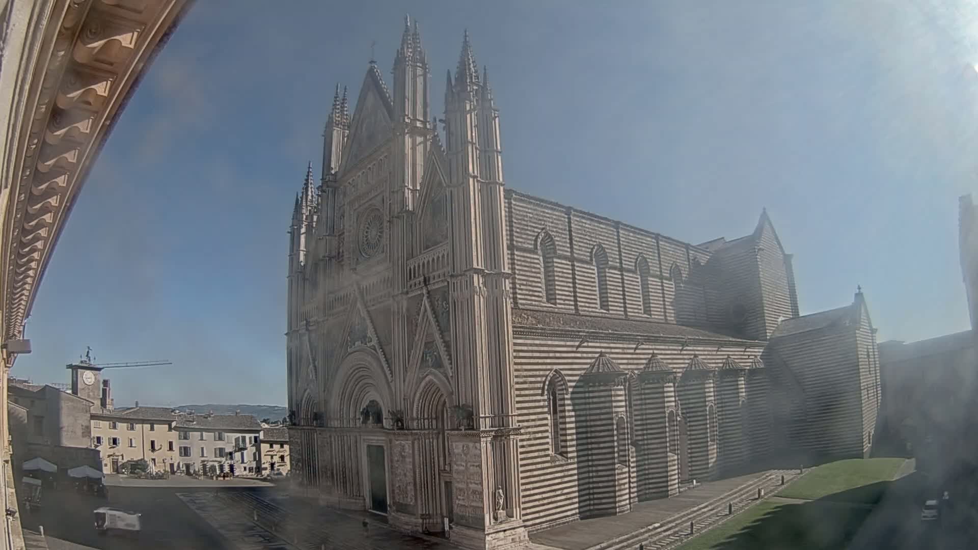 A large, striped cathedral stands in a town square on a hazy, sunny day.