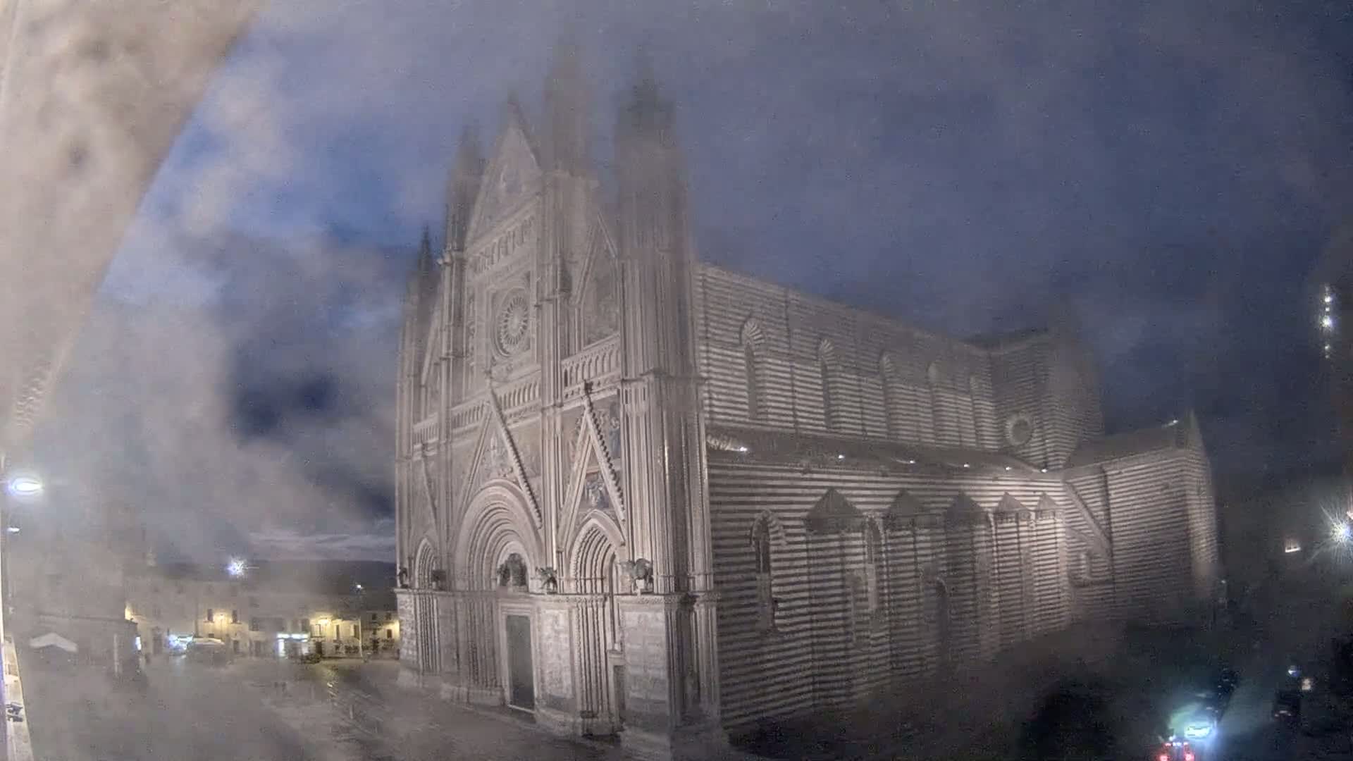A large, striped cathedral stands in a town square at night under a foggy sky.