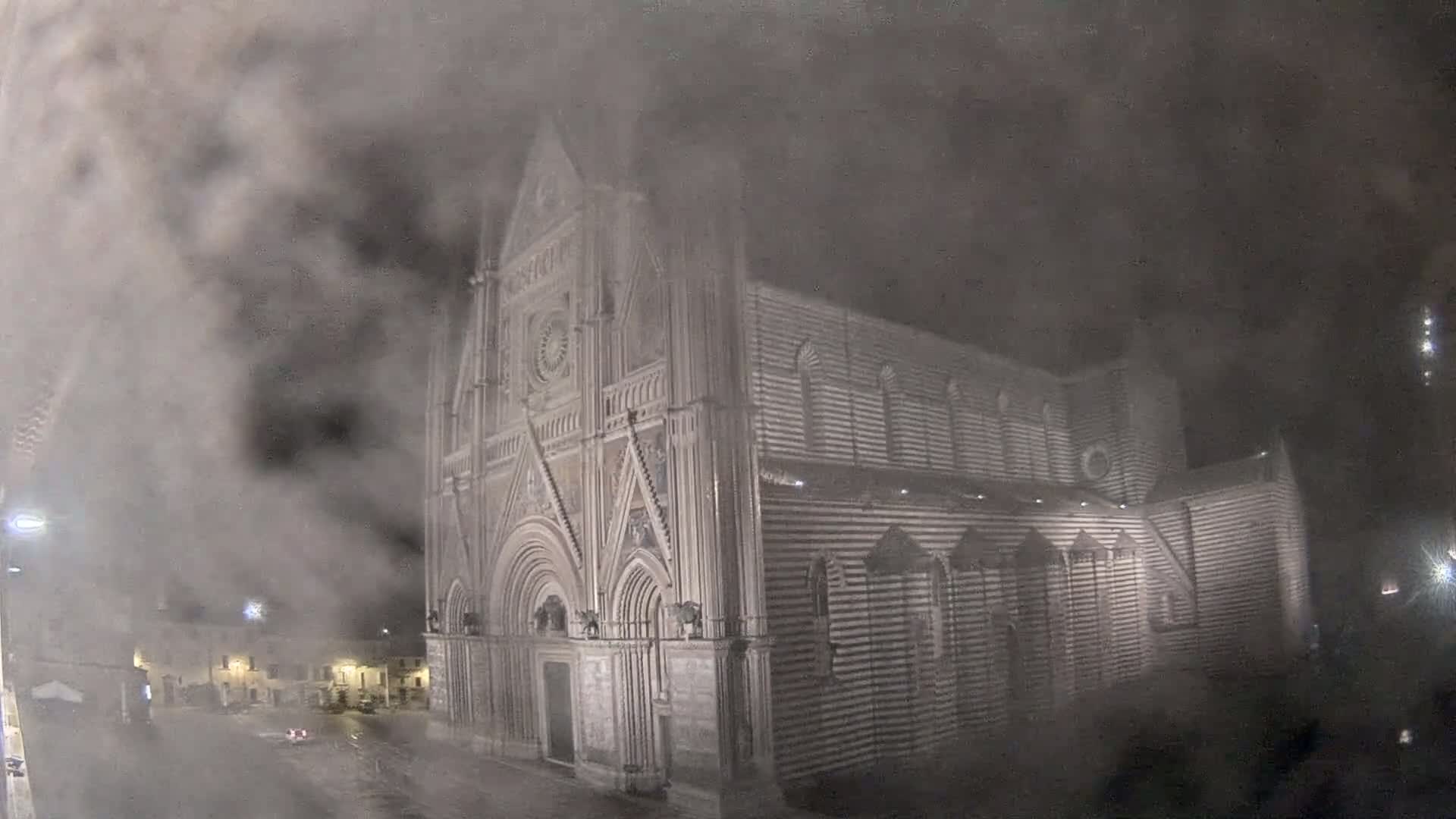 A large, striped stone cathedral is partially obscured by heavy fog or mist at night.