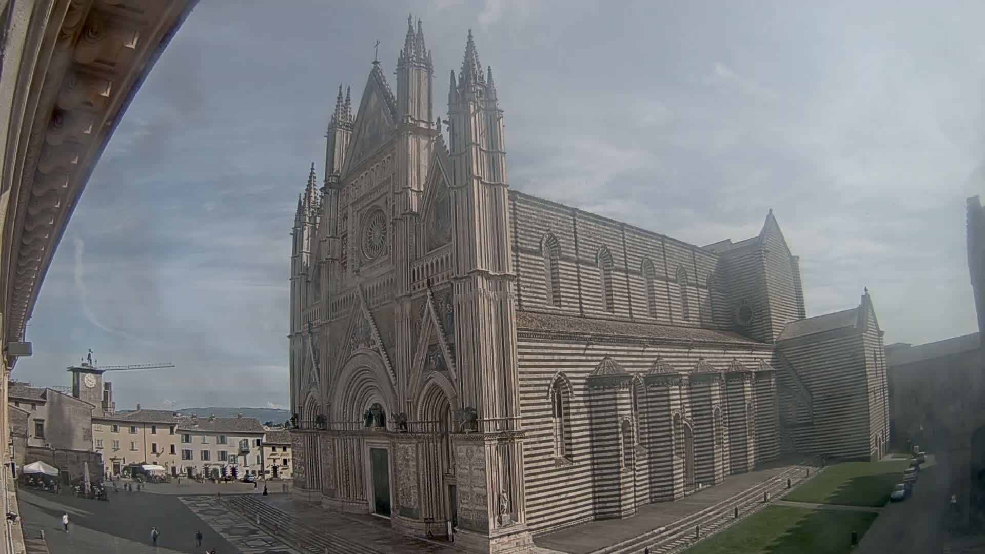 A large, striped stone cathedral stands in a town square on a partly cloudy day.
