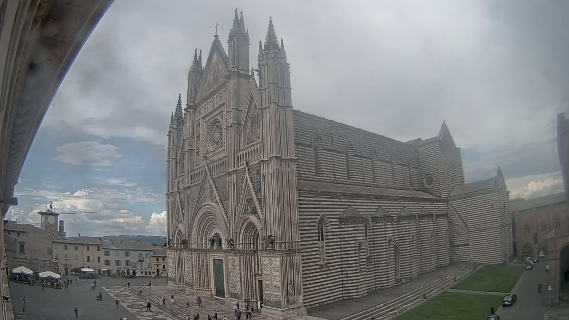 A large, striped cathedral stands in a town square under a cloudy sky.