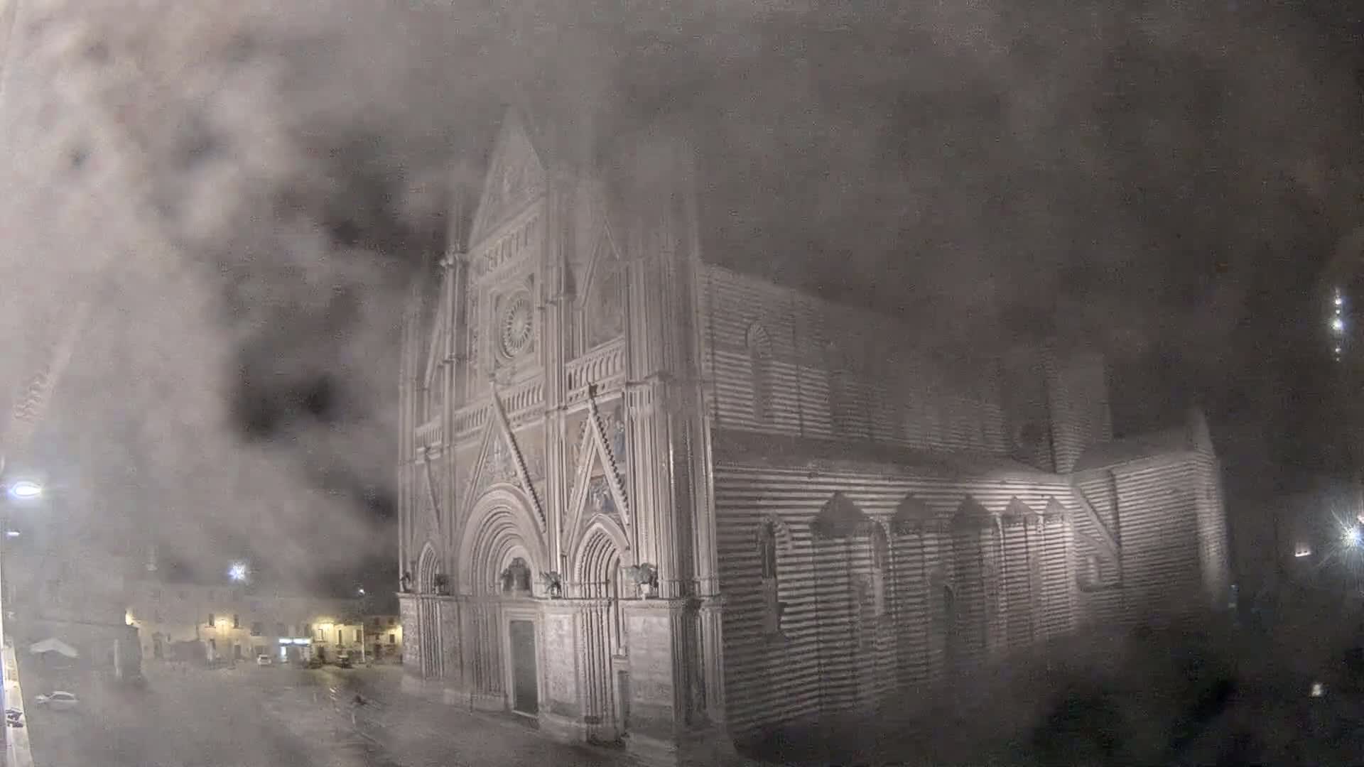 A large, striped stone cathedral is partially obscured by heavy fog or mist at night.