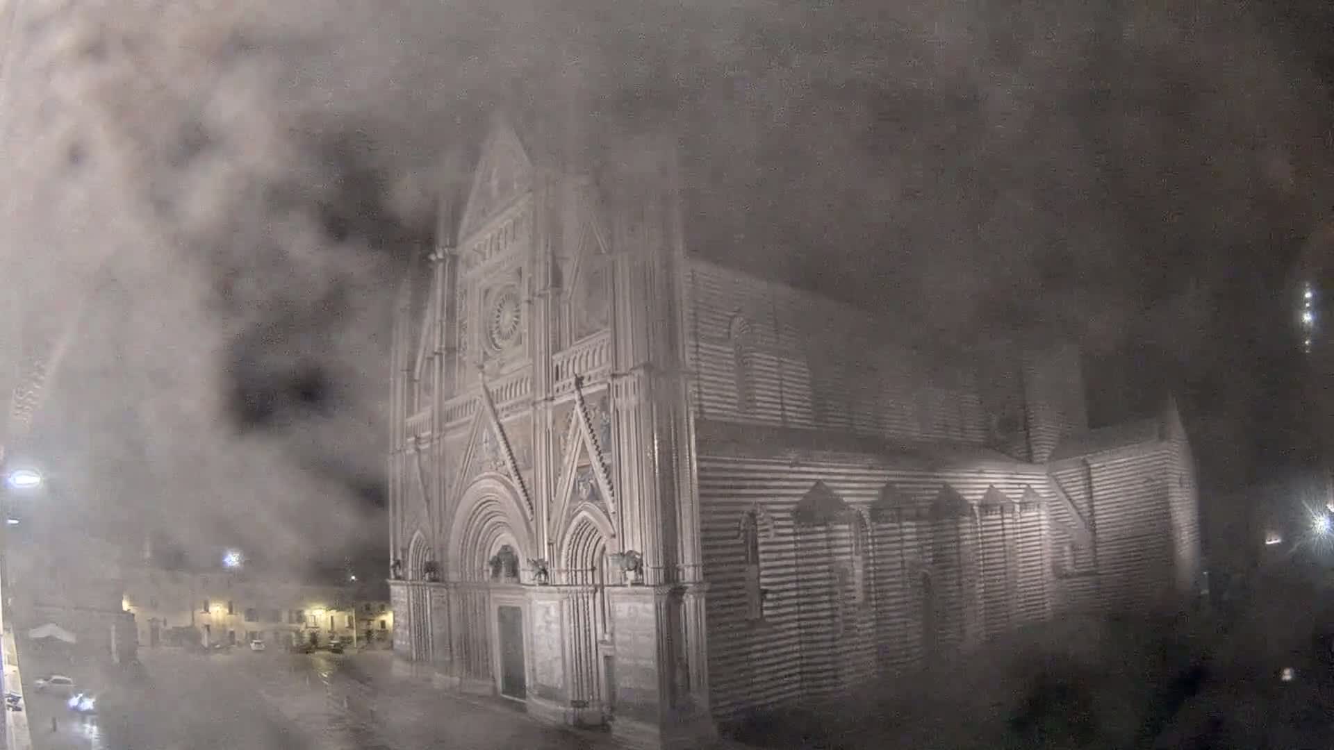 A large, striped stone cathedral is partially obscured by heavy fog or mist at night.