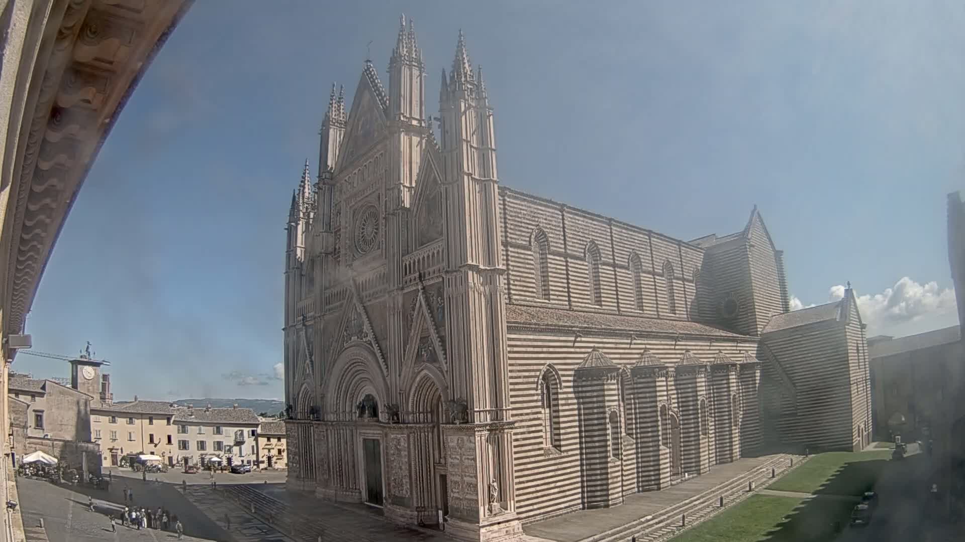 A large, striped stone cathedral stands in a town square on a sunny day.