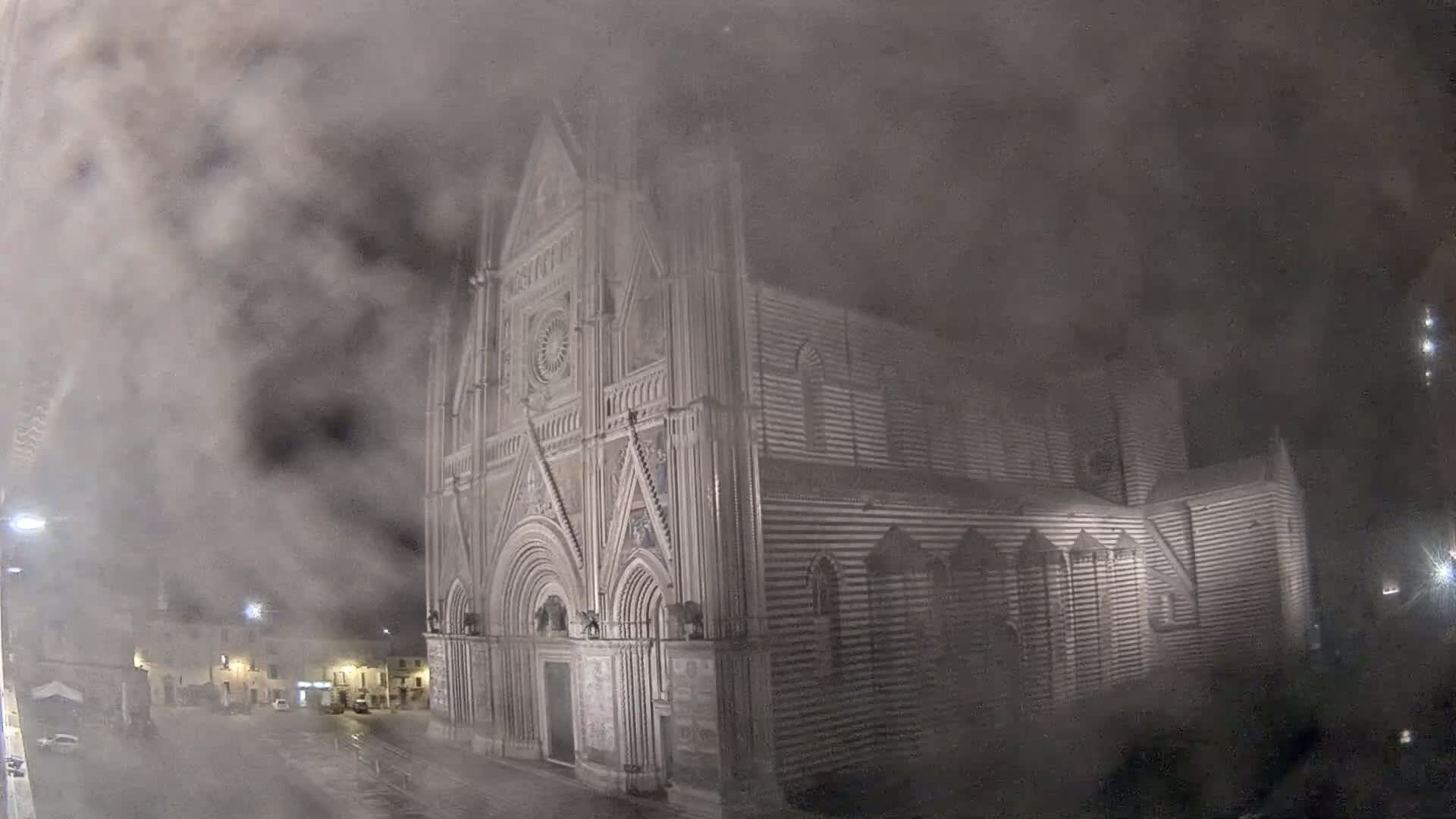 A large, striped stone cathedral stands in a town square at night, obscured by heavy fog or snow.