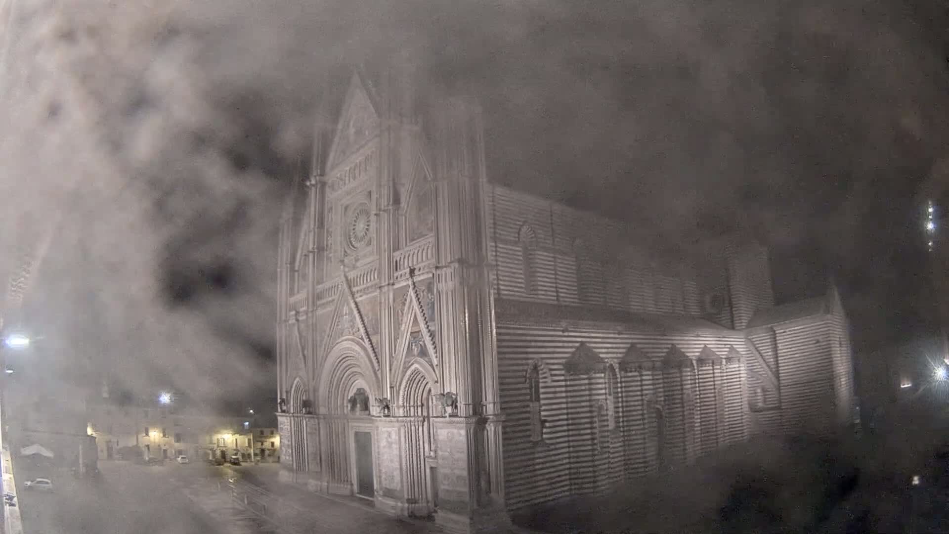 A large, striped stone cathedral is partially obscured by a thick fog at night.