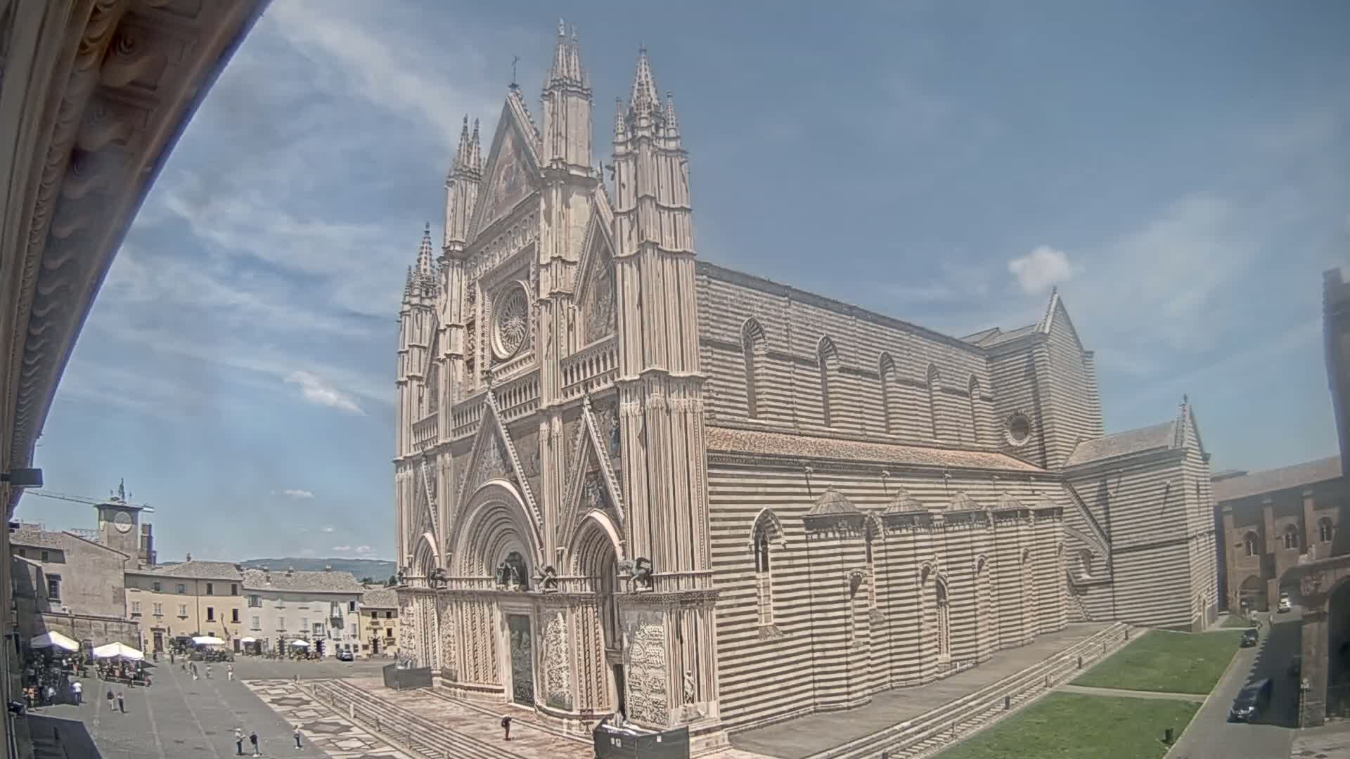 A large, striped stone cathedral stands in a town square on a partly sunny day.