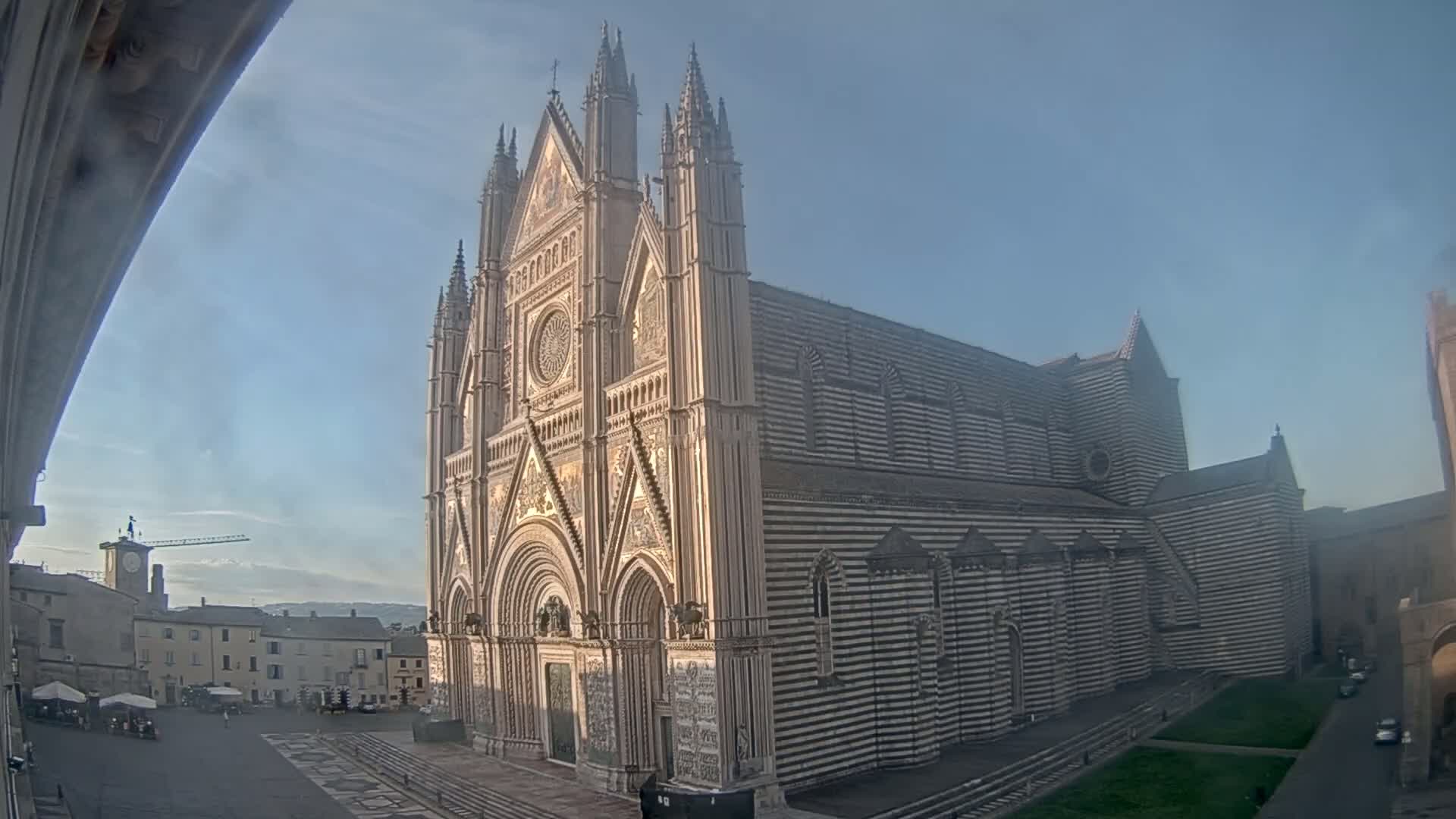 A large, ornate cathedral with striped exterior walls stands in a town square on a clear, sunny day.
