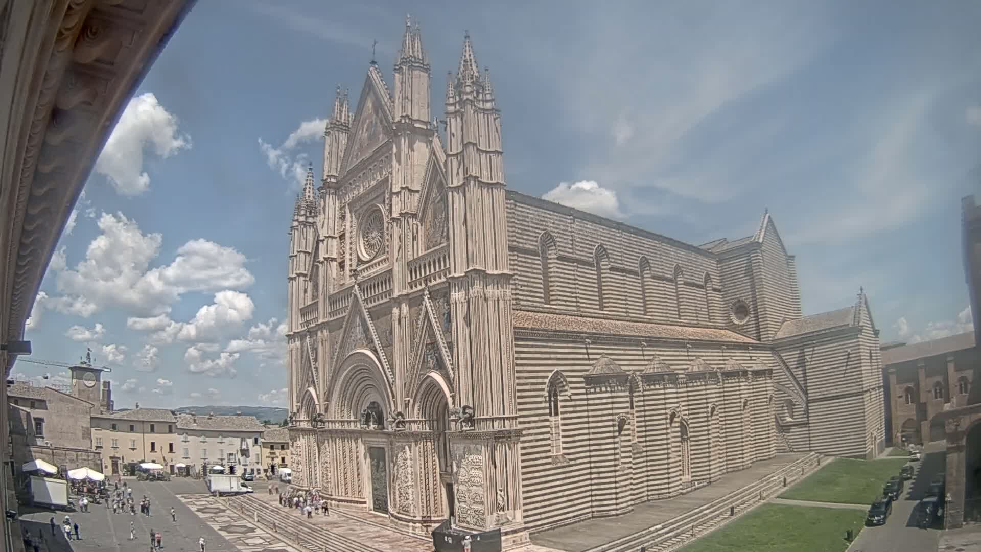 A large, striped stone cathedral stands in a town square on a partly cloudy day.