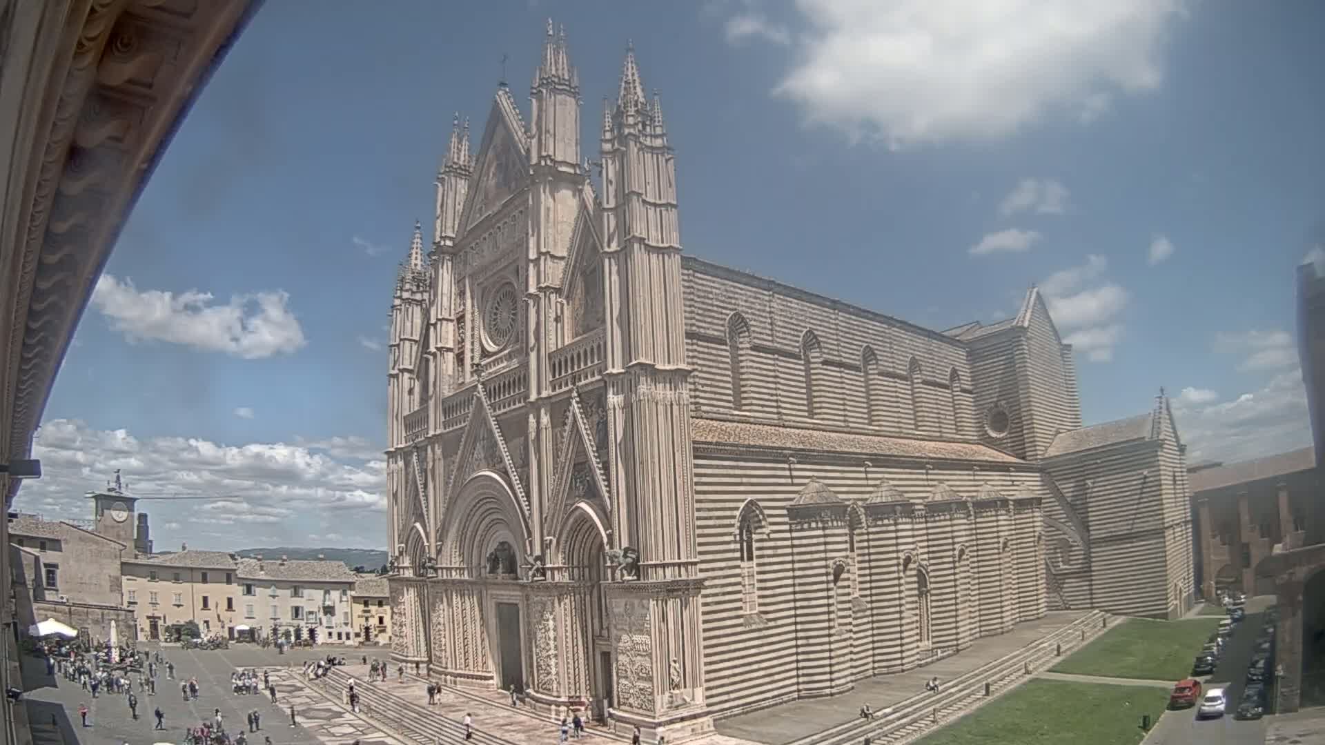 A large, striped stone cathedral stands in a town square on a partly cloudy day.