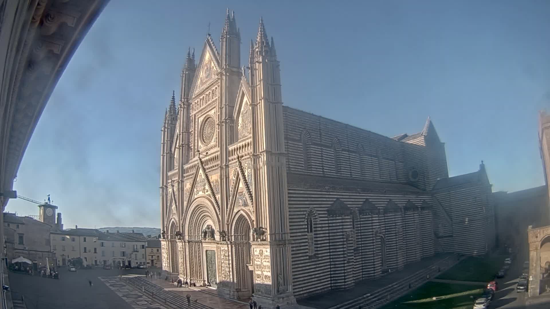 A large, ornate cathedral with striped facade stands in a town square on a clear, sunny day.