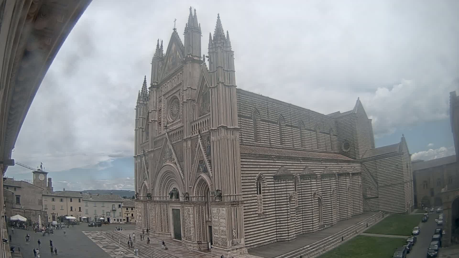A large, striped stone cathedral stands in a town square on an overcast day.