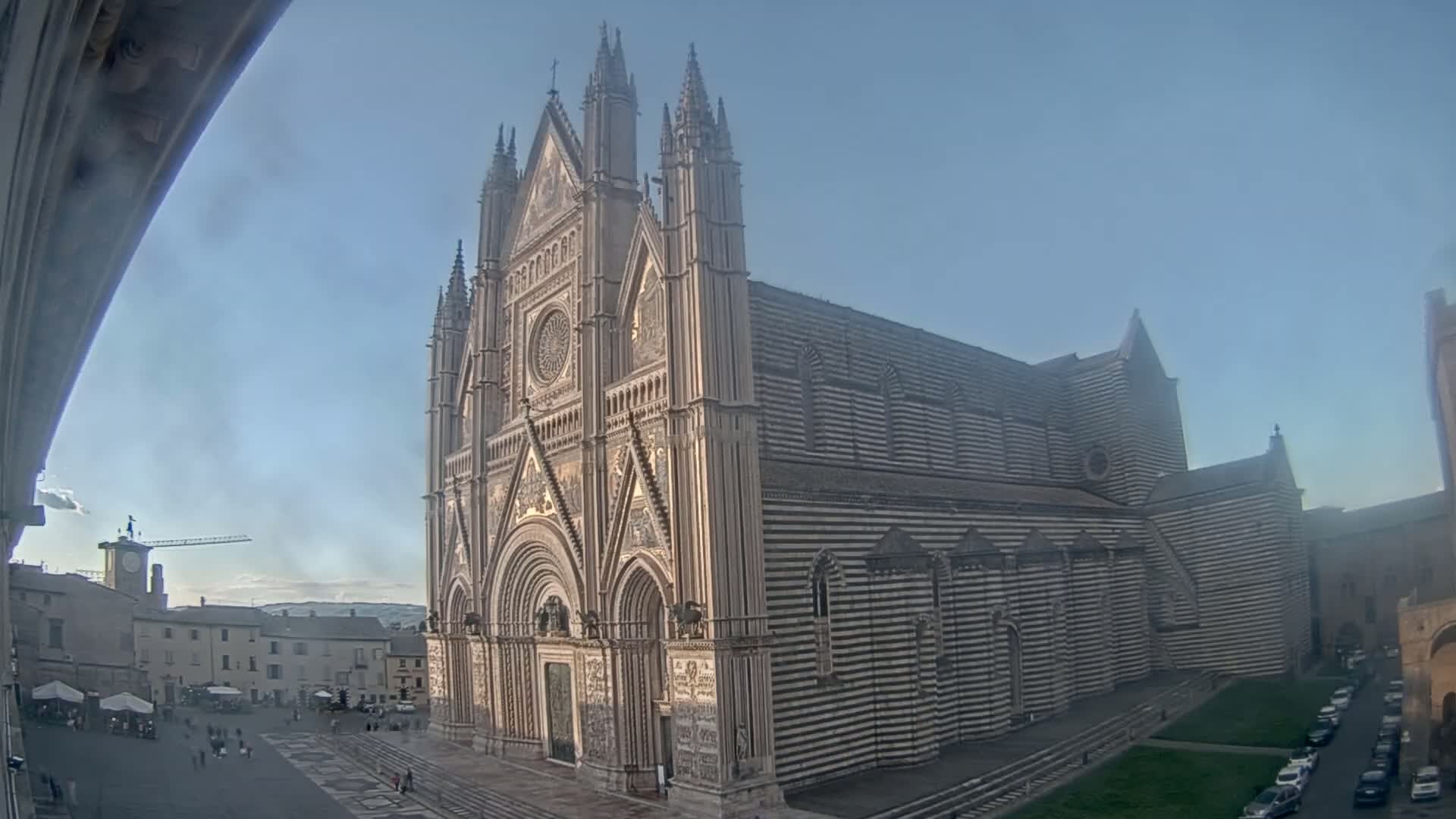 A large, striped cathedral stands in a city square under a clear, light blue sky.