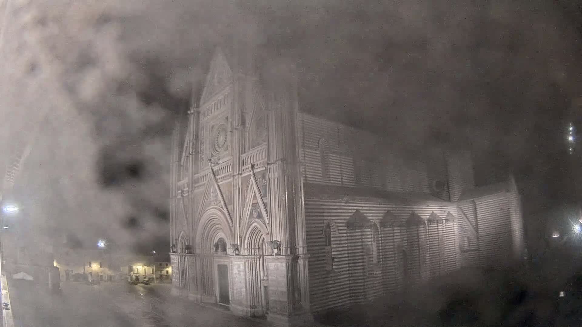 A large stone cathedral is partially obscured by heavy fog at night.