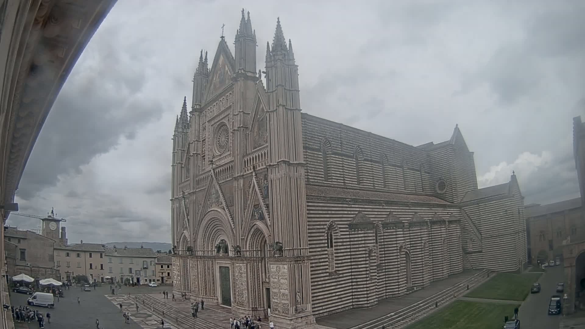 A large, striped stone cathedral stands in a city square under an overcast sky.