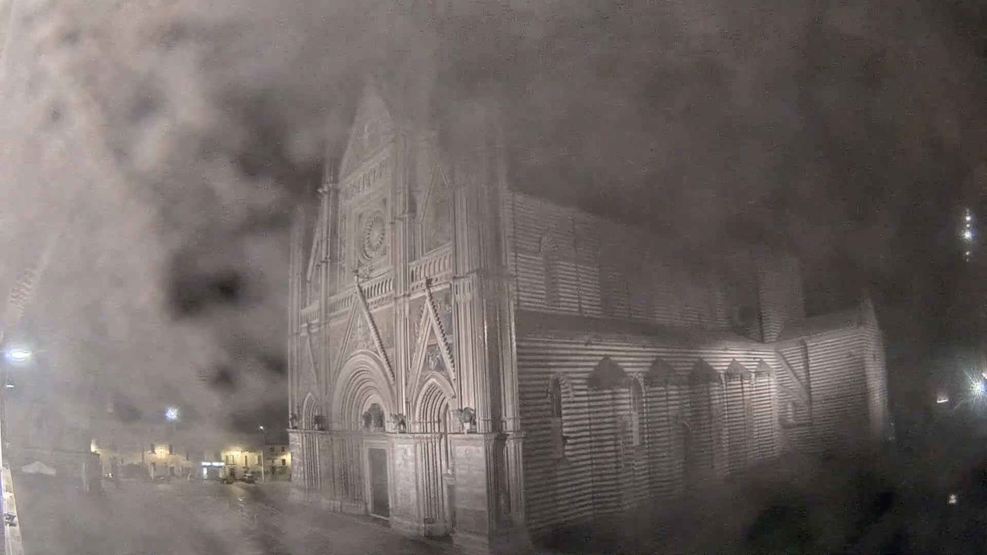 A large, striped stone church is partially obscured by a thick fog at night.