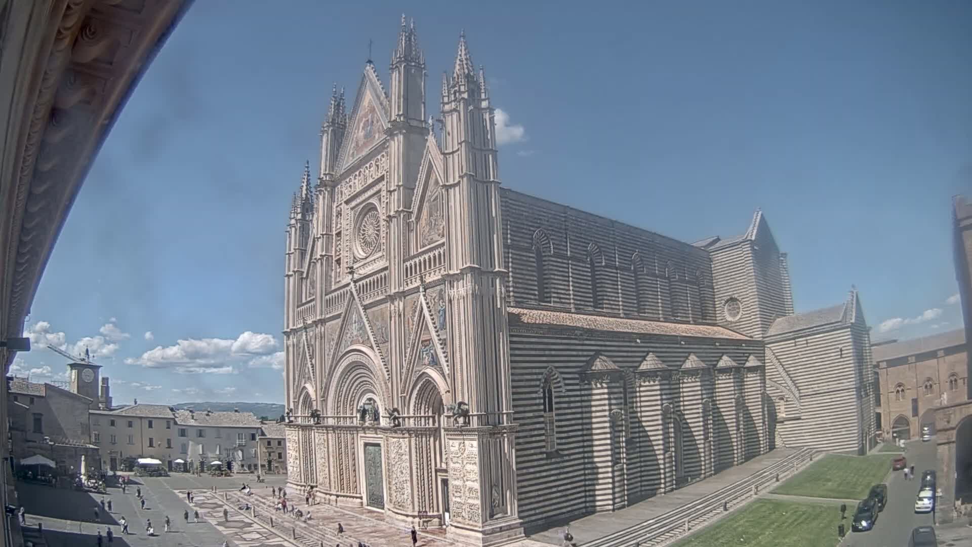 A large, ornate cathedral with striped stonework stands in a town square on a partly sunny day.