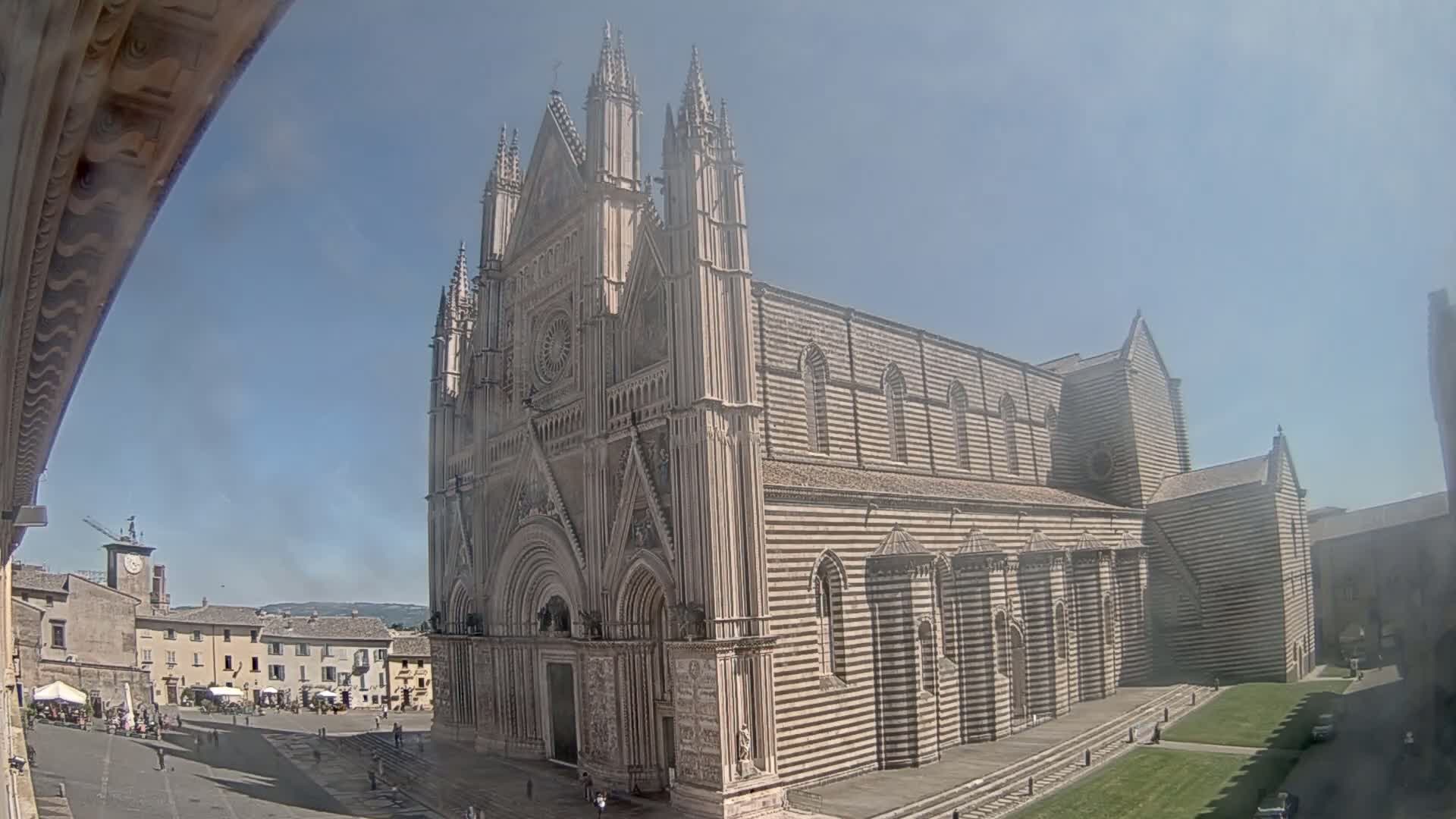 A large striped cathedral stands in a town square on a sunny day.