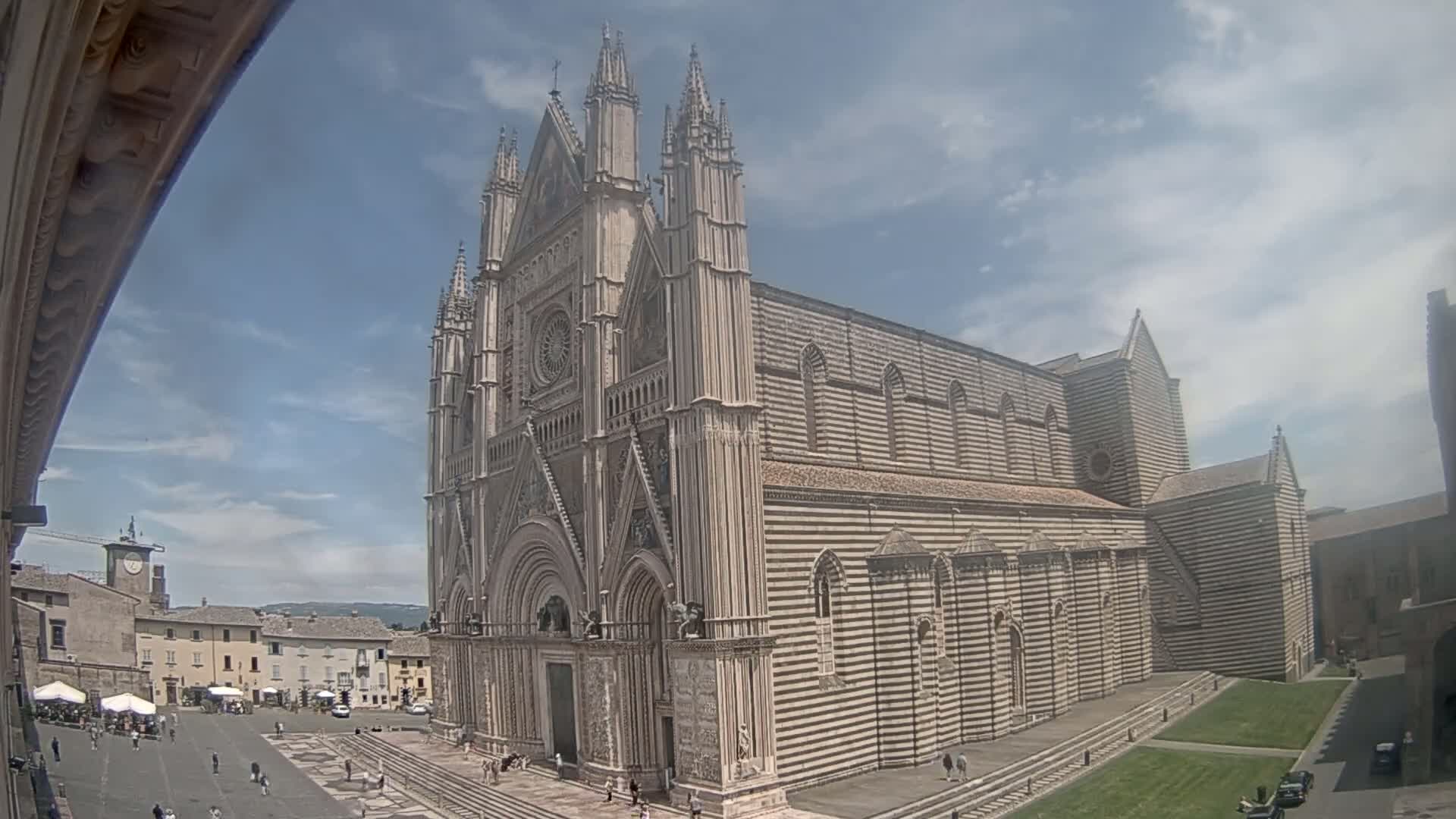 A large, striped stone cathedral stands in a town square on a partly cloudy day.