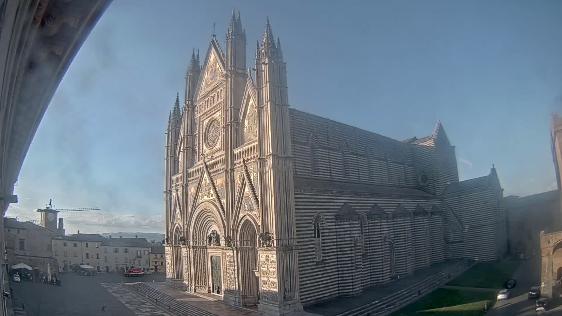 A large, ornate cathedral with black and white striped exterior stands in a town square on a clear, sunny day.