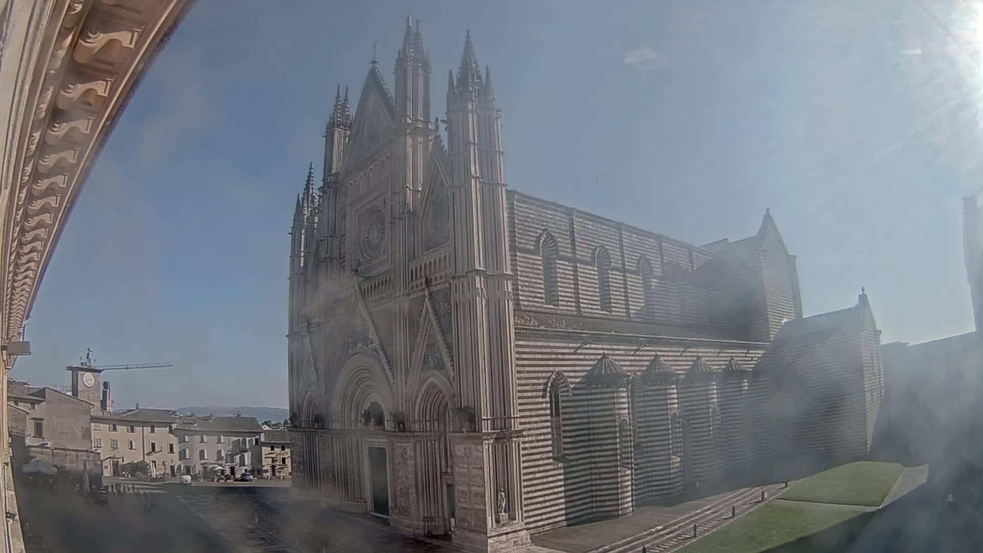 A large, striped stone cathedral stands in a hazy, sunny town square.