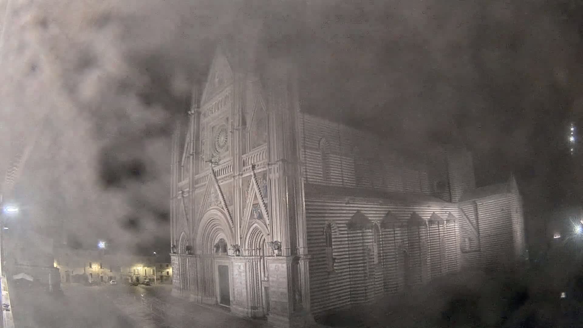 A large, striped stone cathedral is partially obscured by heavy fog at night.