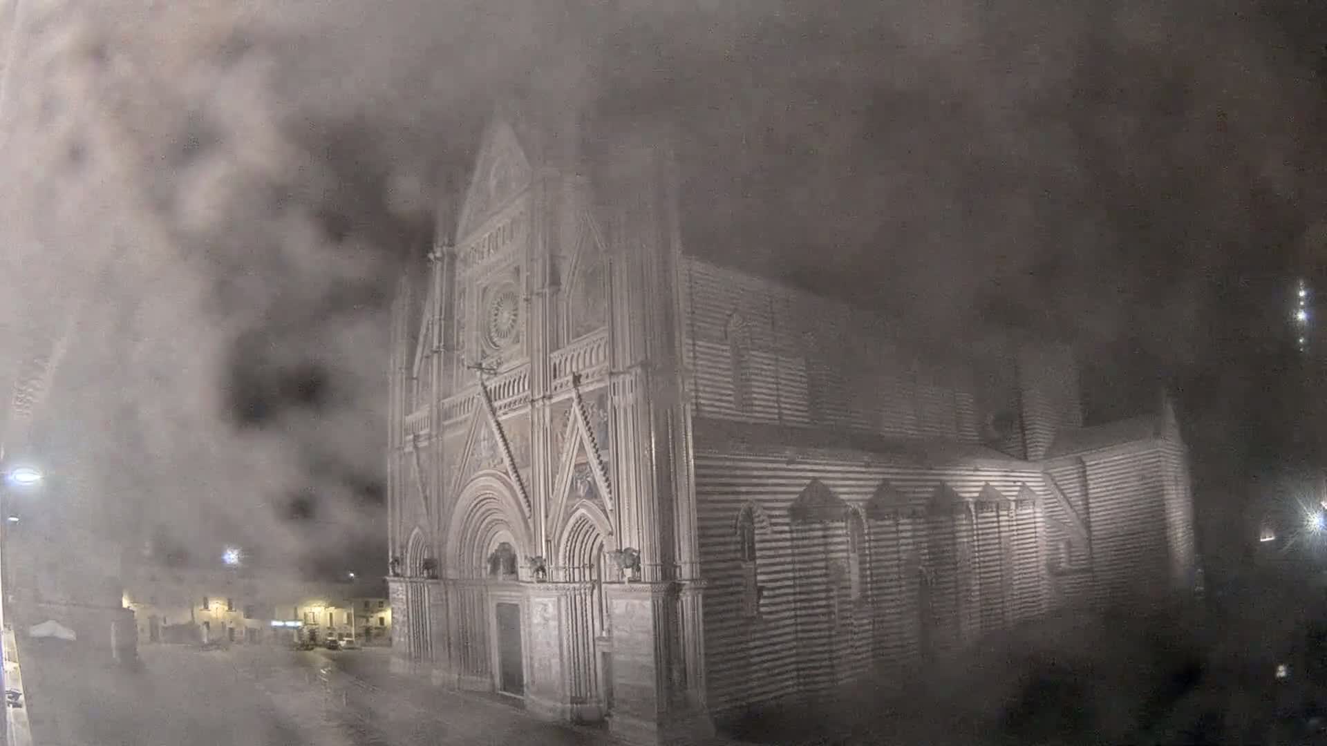 A large, striped stone cathedral is partially obscured by heavy fog at night.
