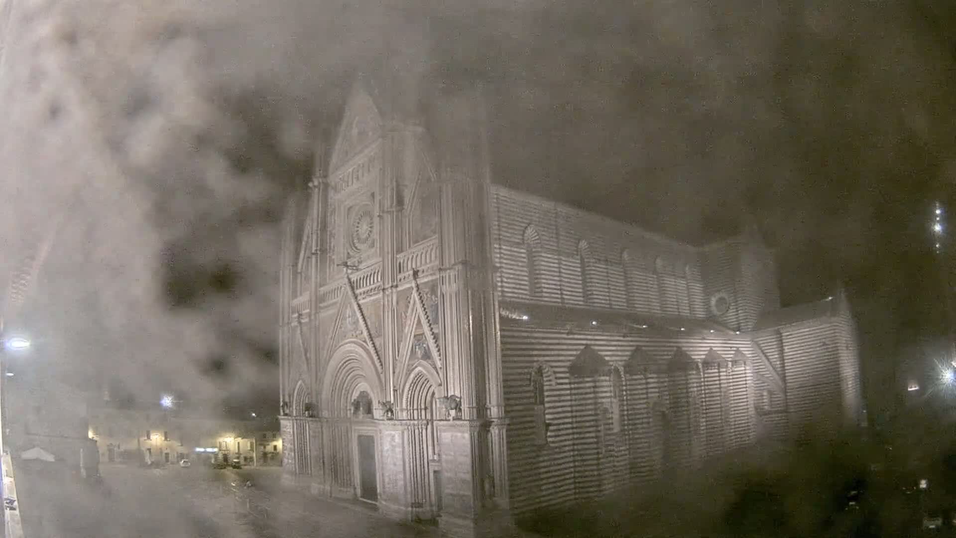 A large, striped stone cathedral is seen at night, partially obscured by a thick fog.
