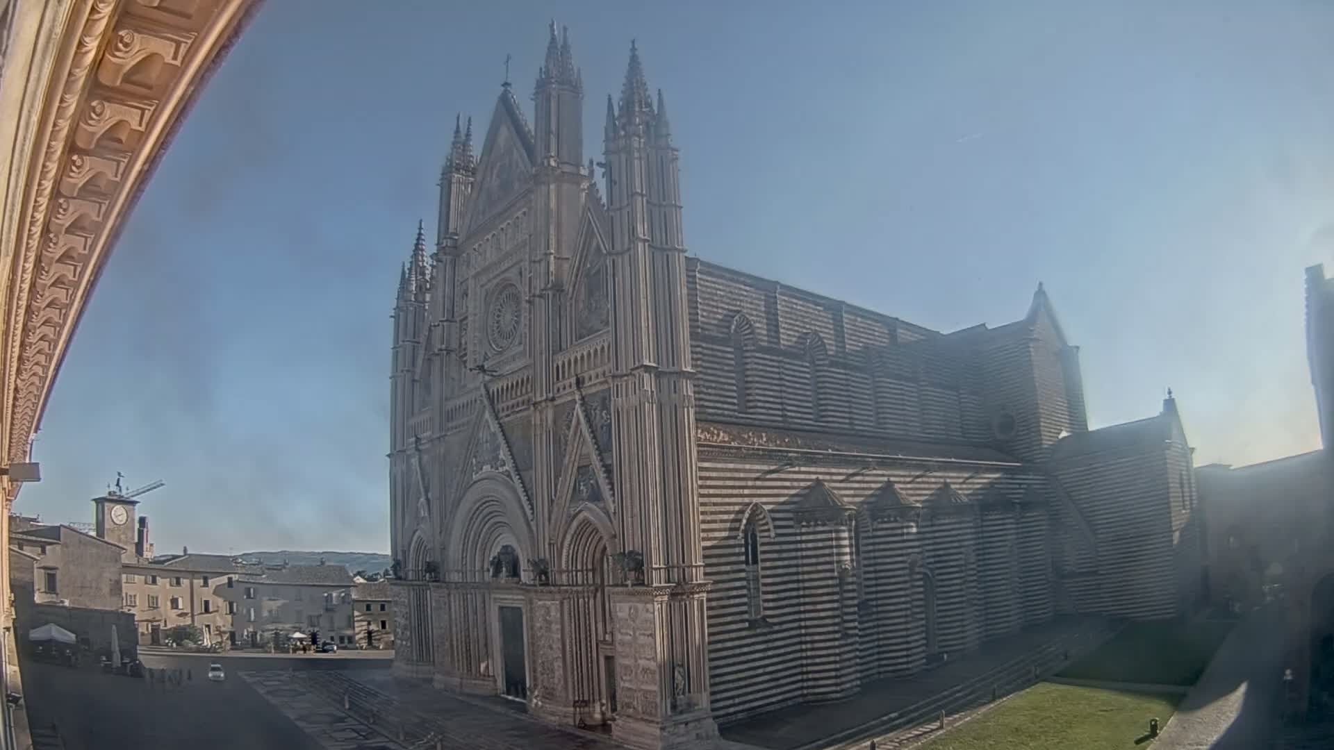 A large, ornate cathedral with striped facade stands in a town square on a clear, sunny day.