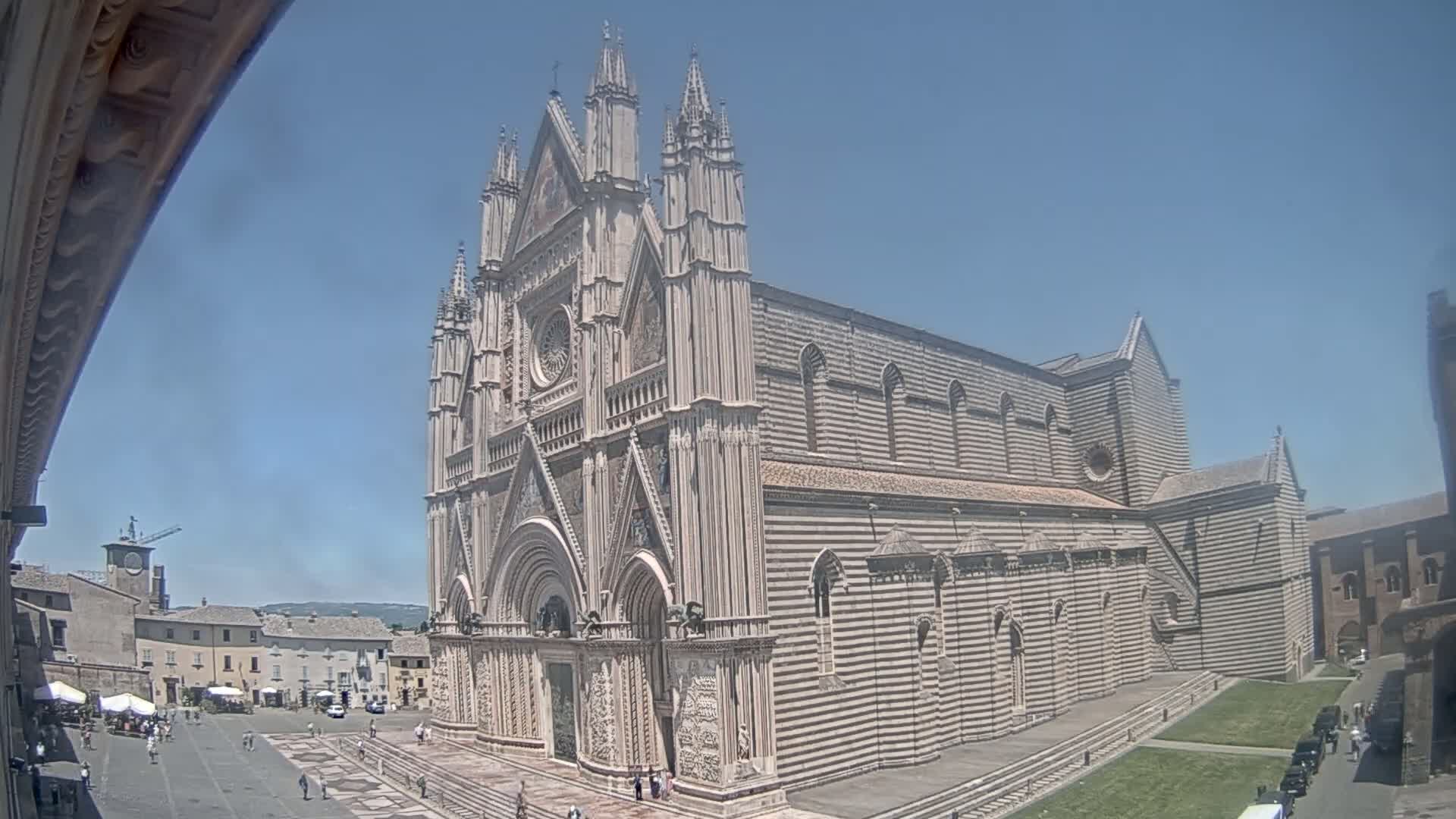A large, ornate cathedral with striped stonework stands in a town square on a clear, sunny day.